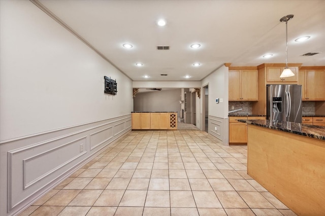 kitchen with light brown cabinetry, tasteful backsplash, decorative light fixtures, dark stone countertops, and stainless steel fridge