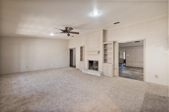 unfurnished living room featuring a fireplace, built in features, ceiling fan, and dark colored carpet