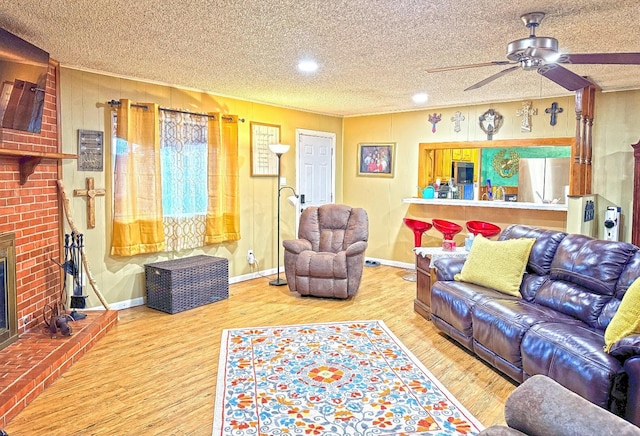 living room with hardwood / wood-style flooring, ceiling fan, a textured ceiling, and a fireplace