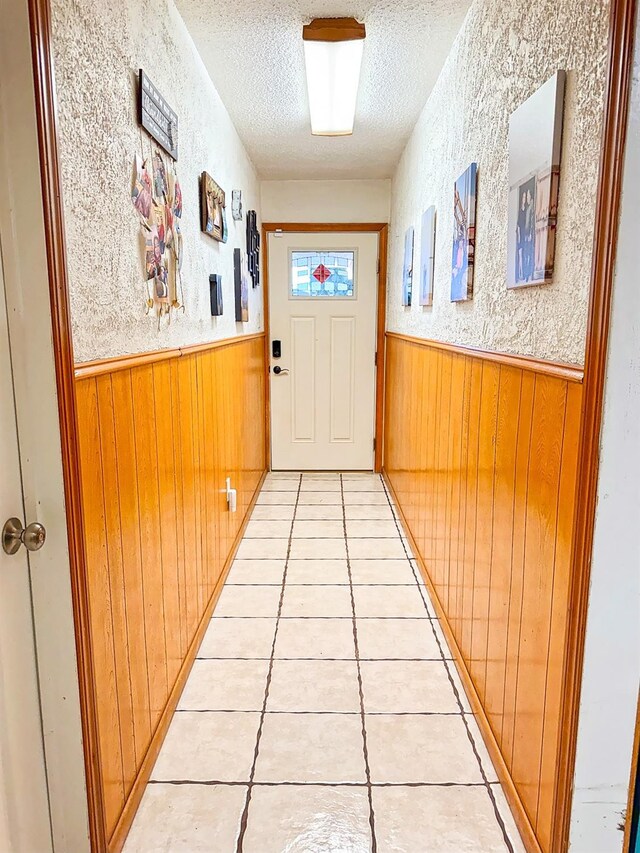 corridor featuring wooden walls, a textured ceiling, and light tile patterned floors