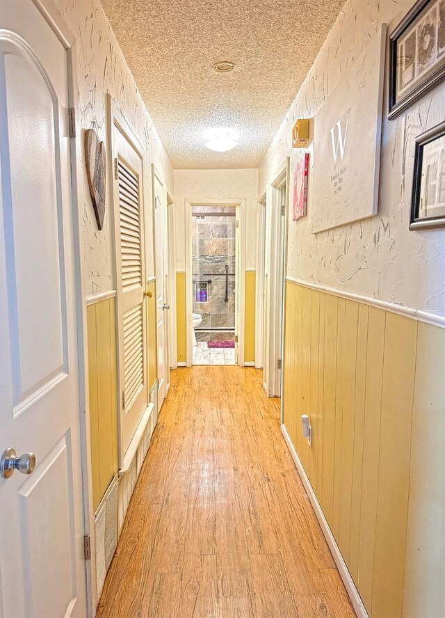 hallway with wood walls, a textured ceiling, and light wood-type flooring