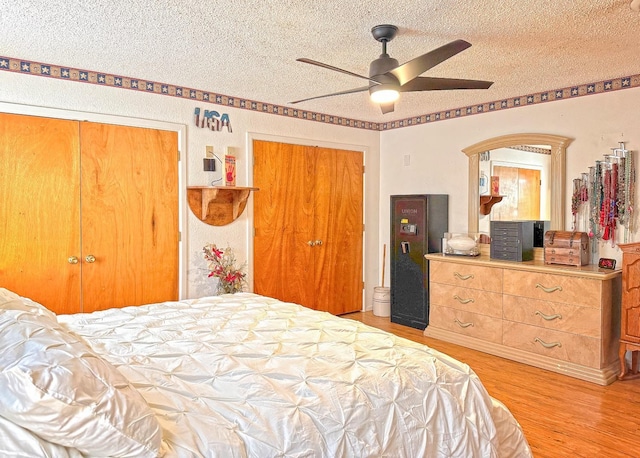 bedroom featuring ceiling fan, two closets, a textured ceiling, and light wood-type flooring