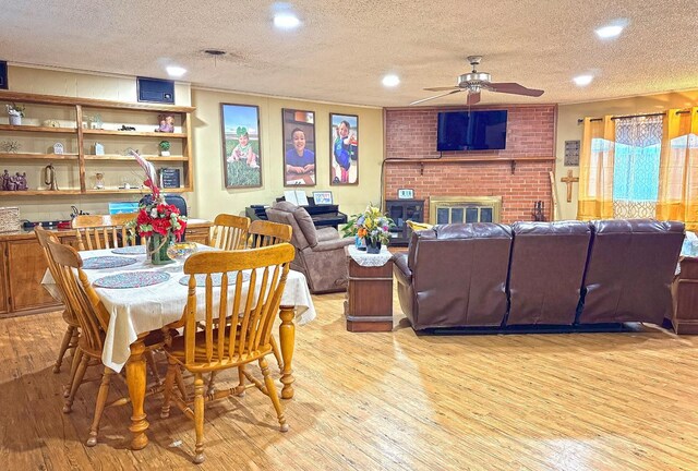 dining room with ceiling fan, a fireplace, a textured ceiling, and light wood-type flooring