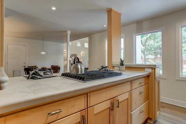 kitchen with light hardwood / wood-style flooring, hanging light fixtures, stainless steel gas cooktop, tile countertops, and ornate columns