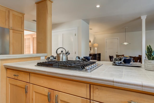 kitchen with pendant lighting, tile countertops, light brown cabinetry, decorative columns, and stainless steel gas stovetop