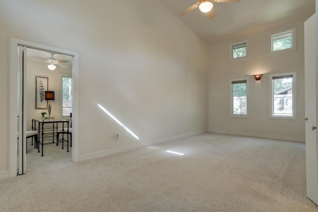 carpeted empty room featuring ceiling fan and a high ceiling