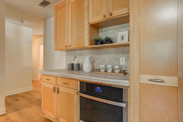 kitchen featuring backsplash, light wood-type flooring, oven, and light brown cabinets