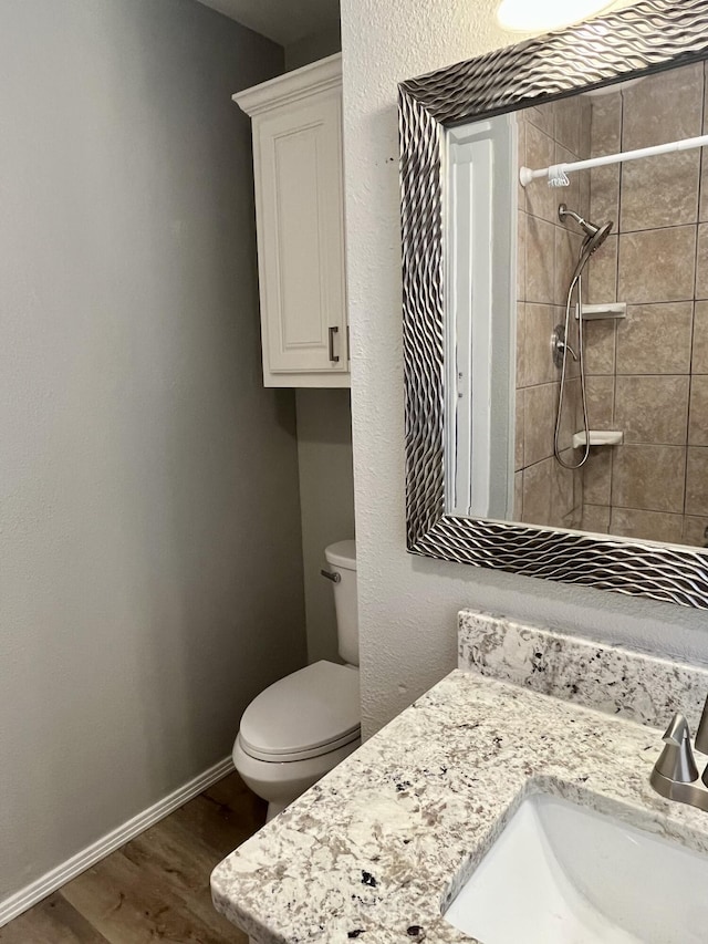 full bathroom featuring toilet, wood finished floors, vanity, baseboards, and tiled shower