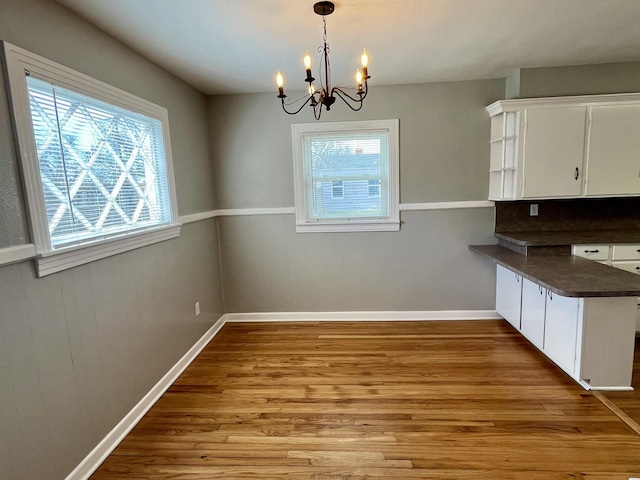 unfurnished dining area featuring a chandelier, wood finished floors, a wealth of natural light, and baseboards