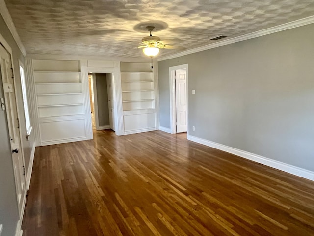 unfurnished room with a textured ceiling, built in shelves, dark wood-style flooring, baseboards, and ornamental molding