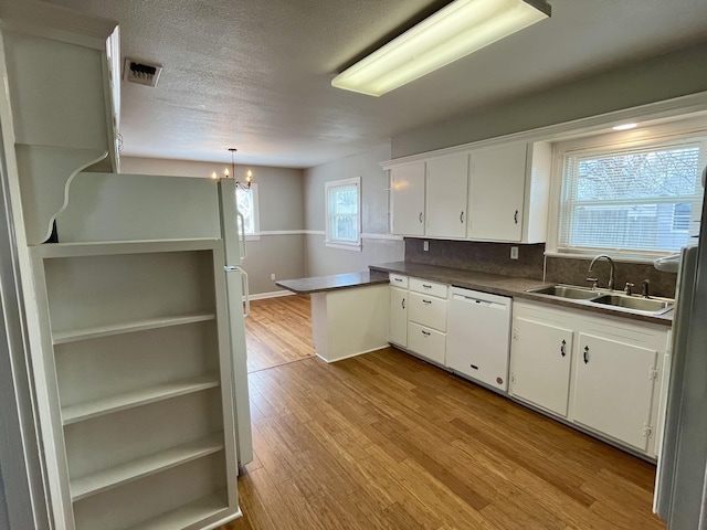 kitchen featuring light wood finished floors, visible vents, white cabinets, dishwasher, and a sink