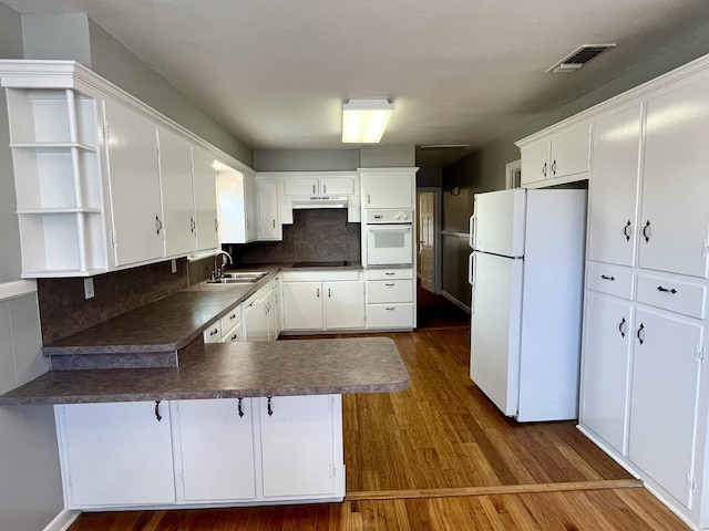 kitchen with open shelves, dark countertops, a sink, white appliances, and a peninsula