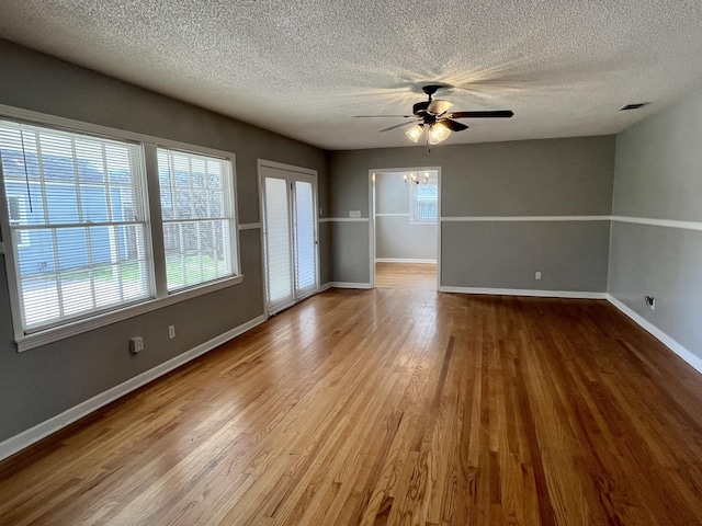 empty room featuring a textured ceiling, ceiling fan with notable chandelier, wood finished floors, visible vents, and baseboards