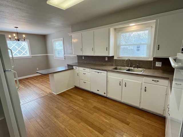 kitchen featuring a peninsula, white appliances, a sink, white cabinets, and light wood-style floors