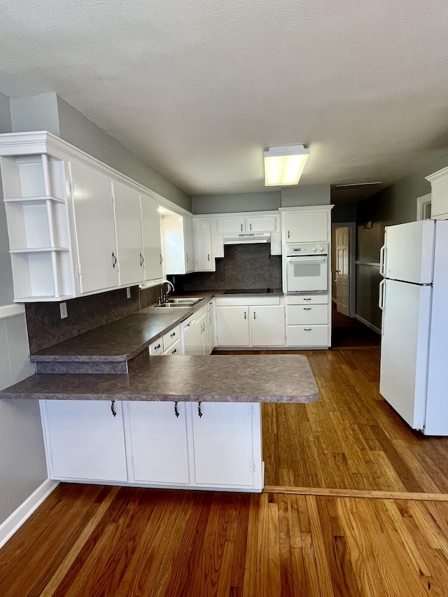 kitchen featuring white appliances, dark wood finished floors, dark countertops, a peninsula, and open shelves