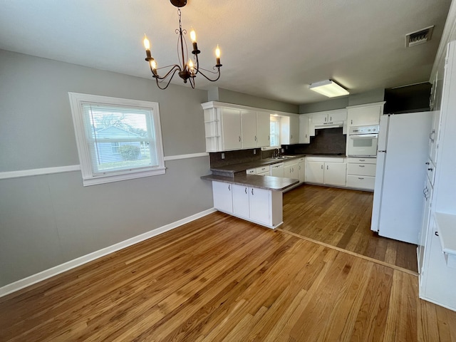 kitchen featuring dark countertops, white cabinets, wood finished floors, white appliances, and a peninsula