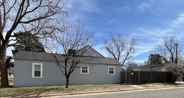 view of side of property with a shingled roof and fence