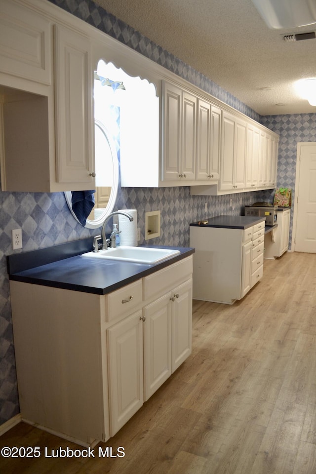 200 Crescent Dr, Littlefield, TX 79339 - kitchen featuring light wood-style flooring, wallpapered walls, visible vents, a sink, and dark countertops