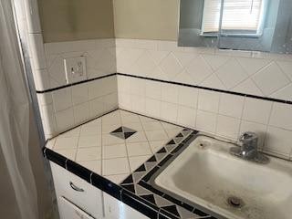 kitchen with tile countertops, sink, and tile walls