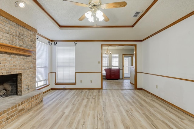 unfurnished living room featuring light hardwood / wood-style floors, a raised ceiling, crown molding, a brick fireplace, and a textured ceiling