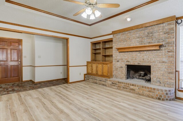 unfurnished living room featuring a textured ceiling, ornamental molding, a raised ceiling, a fireplace, and light hardwood / wood-style floors