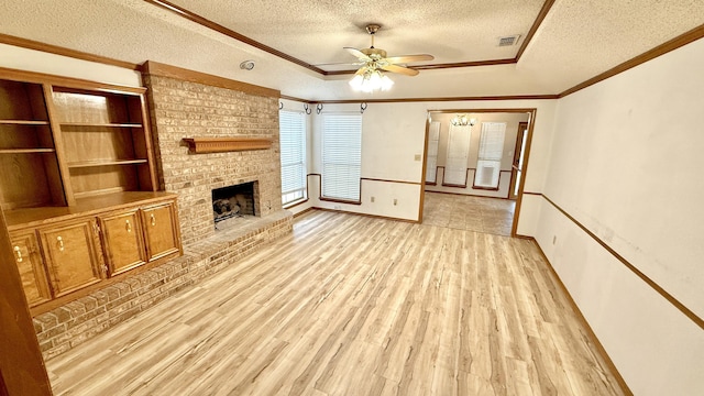 unfurnished living room featuring light wood-type flooring, ceiling fan, crown molding, a brick fireplace, and a textured ceiling