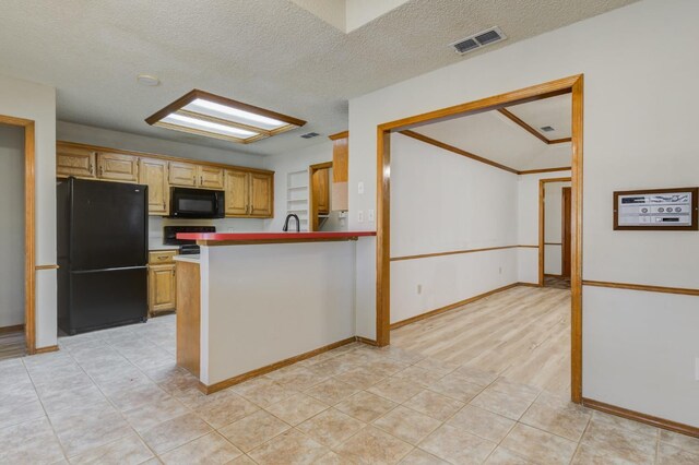 kitchen with light tile patterned floors, black appliances, a textured ceiling, light brown cabinetry, and kitchen peninsula