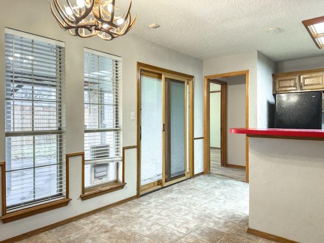 interior space featuring black fridge, a notable chandelier, hanging light fixtures, and a textured ceiling