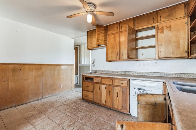 kitchen with ceiling fan, white dishwasher, sink, and wood walls