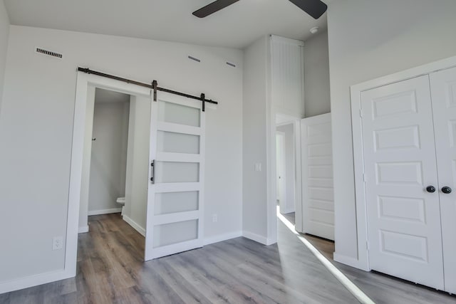 unfurnished bedroom with visible vents, wood finished floors, a barn door, and baseboards
