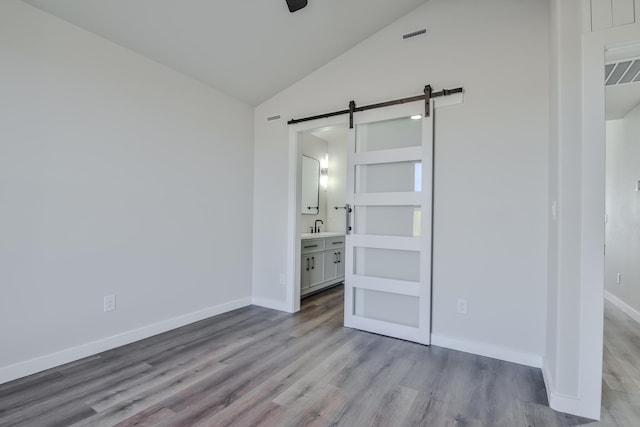 unfurnished bedroom featuring a barn door, wood finished floors, ensuite bath, baseboards, and lofted ceiling