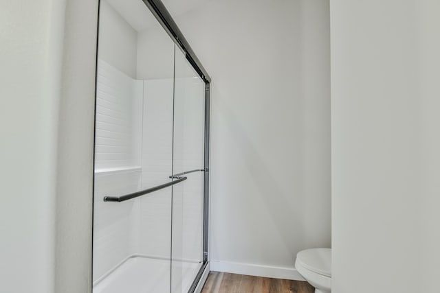 full bathroom featuring baseboards, wood finished floors, a shower stall, and toilet