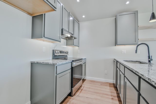 kitchen with a sink, under cabinet range hood, stainless steel electric range oven, light stone counters, and gray cabinetry
