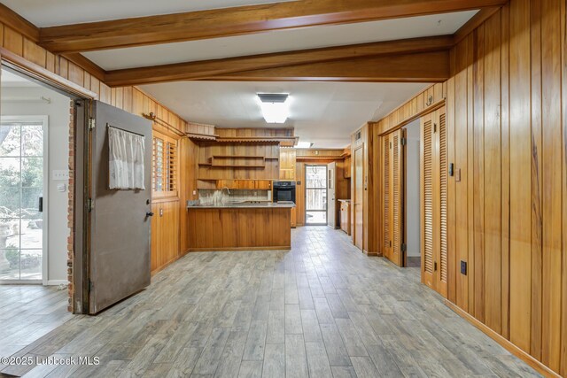 3413 42nd St, Lubbock, TX 79413 - kitchen featuring black oven, beam ceiling, brown cabinetry, a peninsula, and wood walls