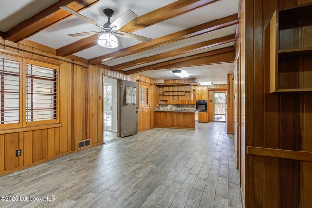 3413 42nd St, Lubbock, TX 79413 - unfurnished living room with beamed ceiling, wood walls, a ceiling fan, light wood-style floors, and a sink