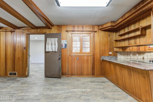 3413 42nd St, Lubbock, TX 79413 - kitchen with brown cabinetry, wood walls, light stone countertops, backsplash, and light wood-style flooring
