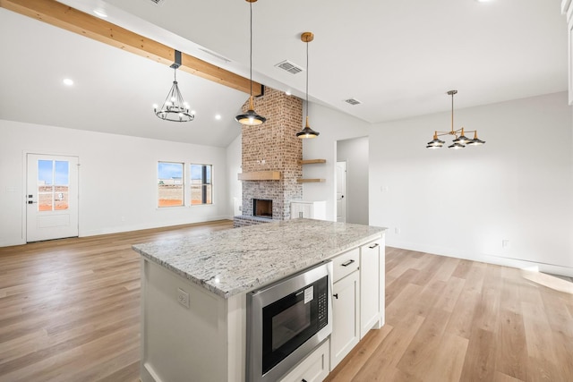 kitchen with black microwave, vaulted ceiling with beams, white cabinets, hanging light fixtures, and a center island