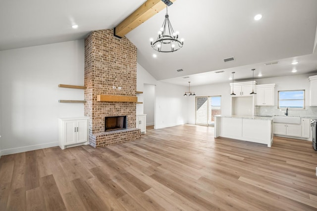 unfurnished living room with sink, a brick fireplace, a notable chandelier, beam ceiling, and light hardwood / wood-style floors