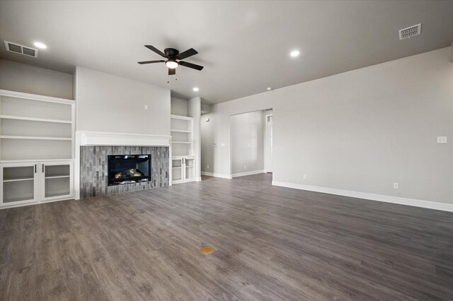 unfurnished living room with dark wood-type flooring, a fireplace, built in shelves, and ceiling fan