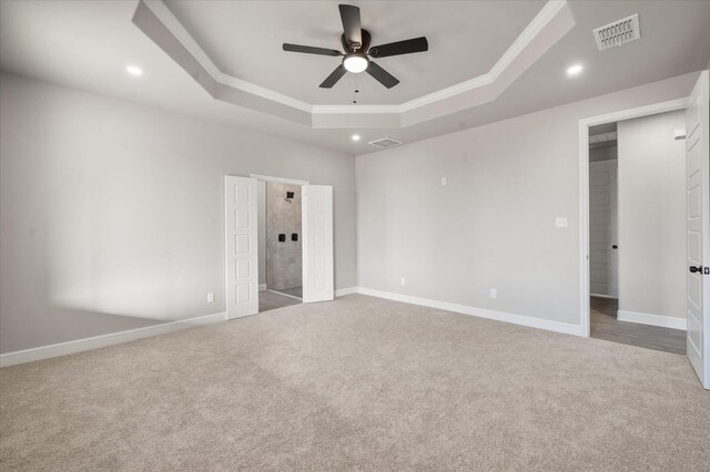 unfurnished bedroom with a tray ceiling, carpet floors, ensuite bath, and ceiling fan