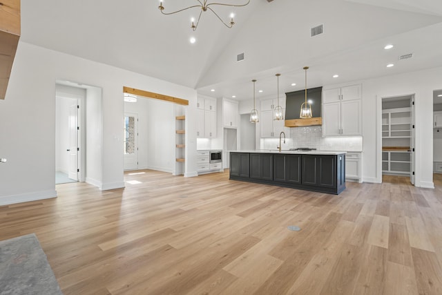 kitchen featuring white cabinetry, custom exhaust hood, a center island with sink, and pendant lighting