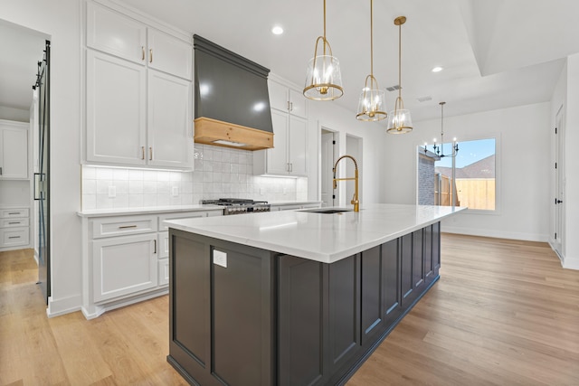 kitchen with pendant lighting, sink, white cabinetry, a center island with sink, and custom exhaust hood