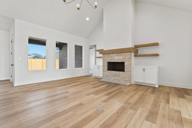 unfurnished living room with high vaulted ceiling, a notable chandelier, a fireplace, and light hardwood / wood-style floors