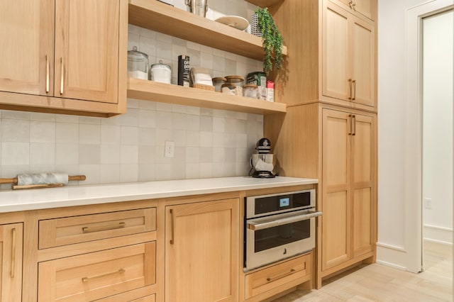 kitchen with tasteful backsplash, stainless steel oven, and light brown cabinetry