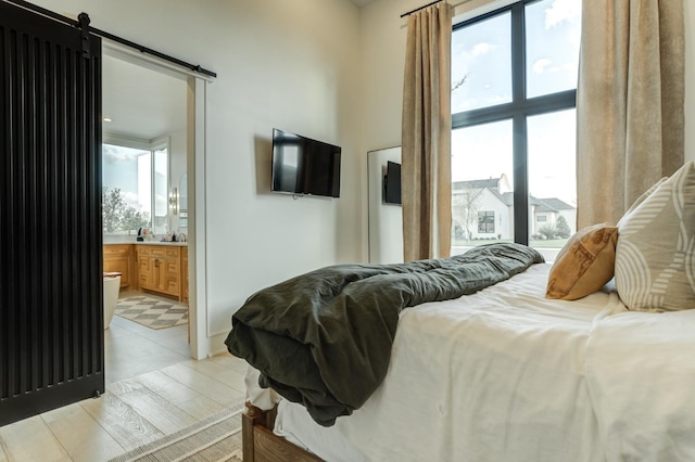 bedroom with ensuite bathroom, a barn door, and light wood-type flooring