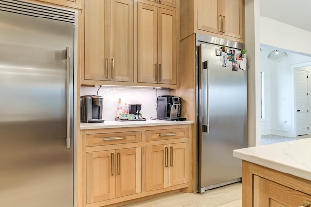 kitchen featuring stainless steel built in refrigerator, high end fridge, light stone counters, and light brown cabinetry