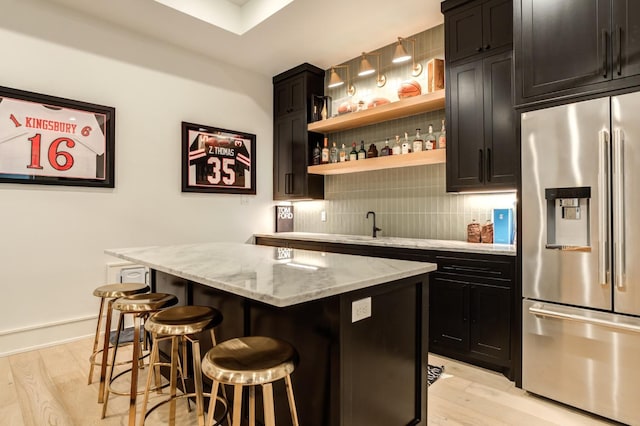 bar with light stone countertops, backsplash, light hardwood / wood-style floors, and stainless steel fridge with ice dispenser