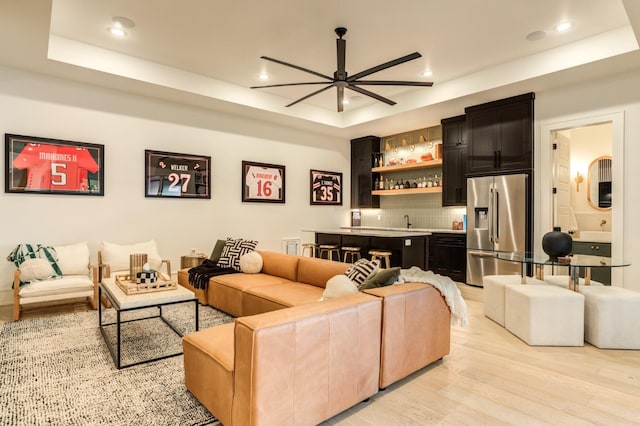 living room with a raised ceiling, ceiling fan, indoor wet bar, and light hardwood / wood-style floors