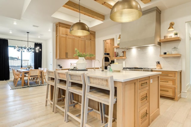 kitchen with light brown cabinetry, light hardwood / wood-style flooring, a center island with sink, custom range hood, and decorative backsplash