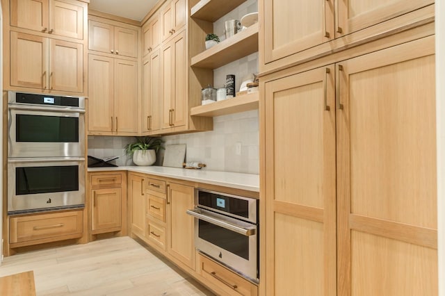 kitchen with stainless steel double oven, light brown cabinetry, decorative backsplash, and light wood-type flooring